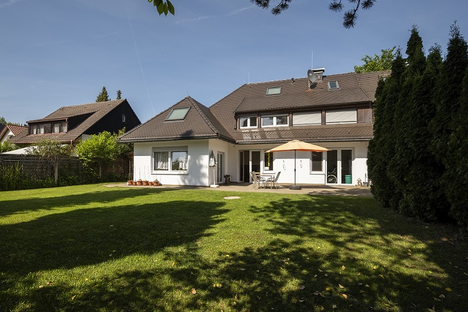 Eine malerische Ansicht der Wohngemeinschaft in der Wiesengrund-Straße in München/Pasing, aufgenommen von einer weitläufigen grünen Rasenfläche aus. Das Bild vermittelt den Eindruck eines großzügigen Gartens, der den Bewohnern Raum für Erholung und Aktivitäten im Freien bietet.