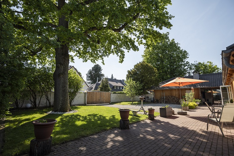 Eine einladende Terrasse oder Außenbereich der Wohngemeinschaft in der Wiesengrund-Straße in München/Pasing, ausgestattet mit einem großen orangefarbenen Sonnenschirm, Tisch und Stühlen. Der Bereich lädt die Bewohner zum Verweilen im Freien und zu gemeinsamen Aktivitäten an der frischen Luft ein.