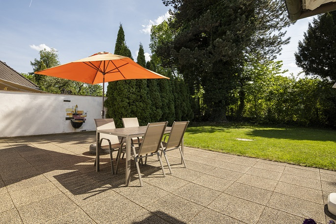 Eine einladende Terrasse oder Außenbereich der Wohngemeinschaft in der Wiesengrund-Straße in München/Pasing, ausgestattet mit einem großen orangefarbenen Sonnenschirm, Tisch und Stühlen. Der Bereich lädt die Bewohner zum Verweilen im Freien und zu gemeinsamen Aktivitäten an der frischen Luft ein.